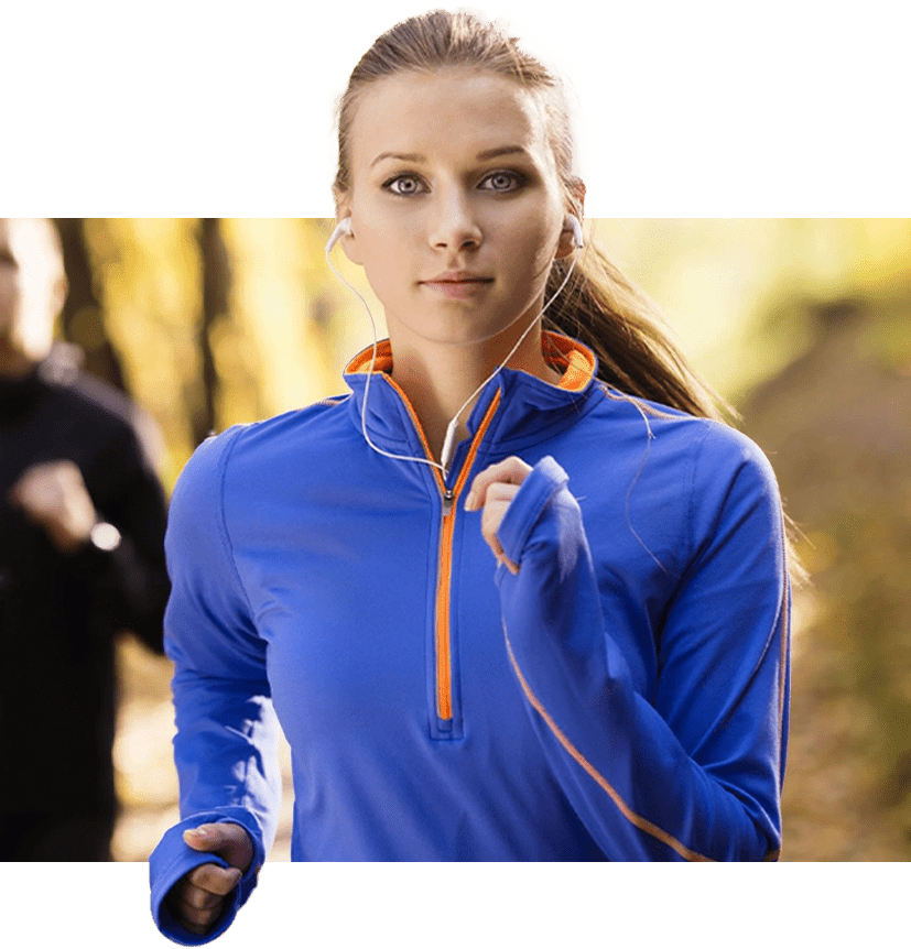 A woman is running in the woods wearing blue and orange.