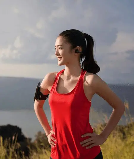 A woman in red shirt holding her hands on the side of her shoulder.